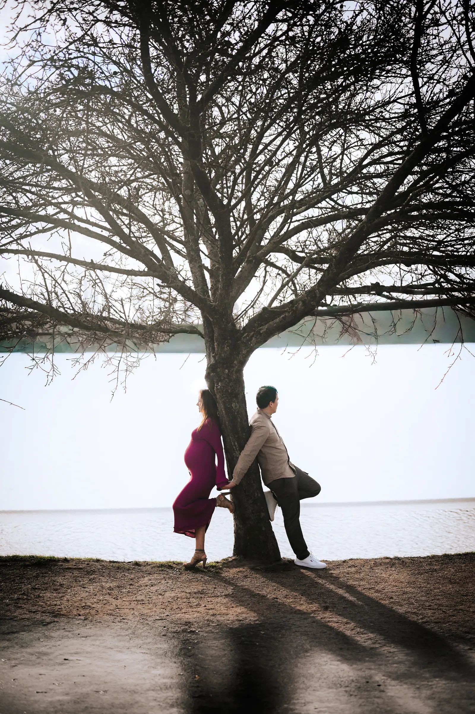 Couple leaning against a tree in front of a white wall, she in a burgundy dress