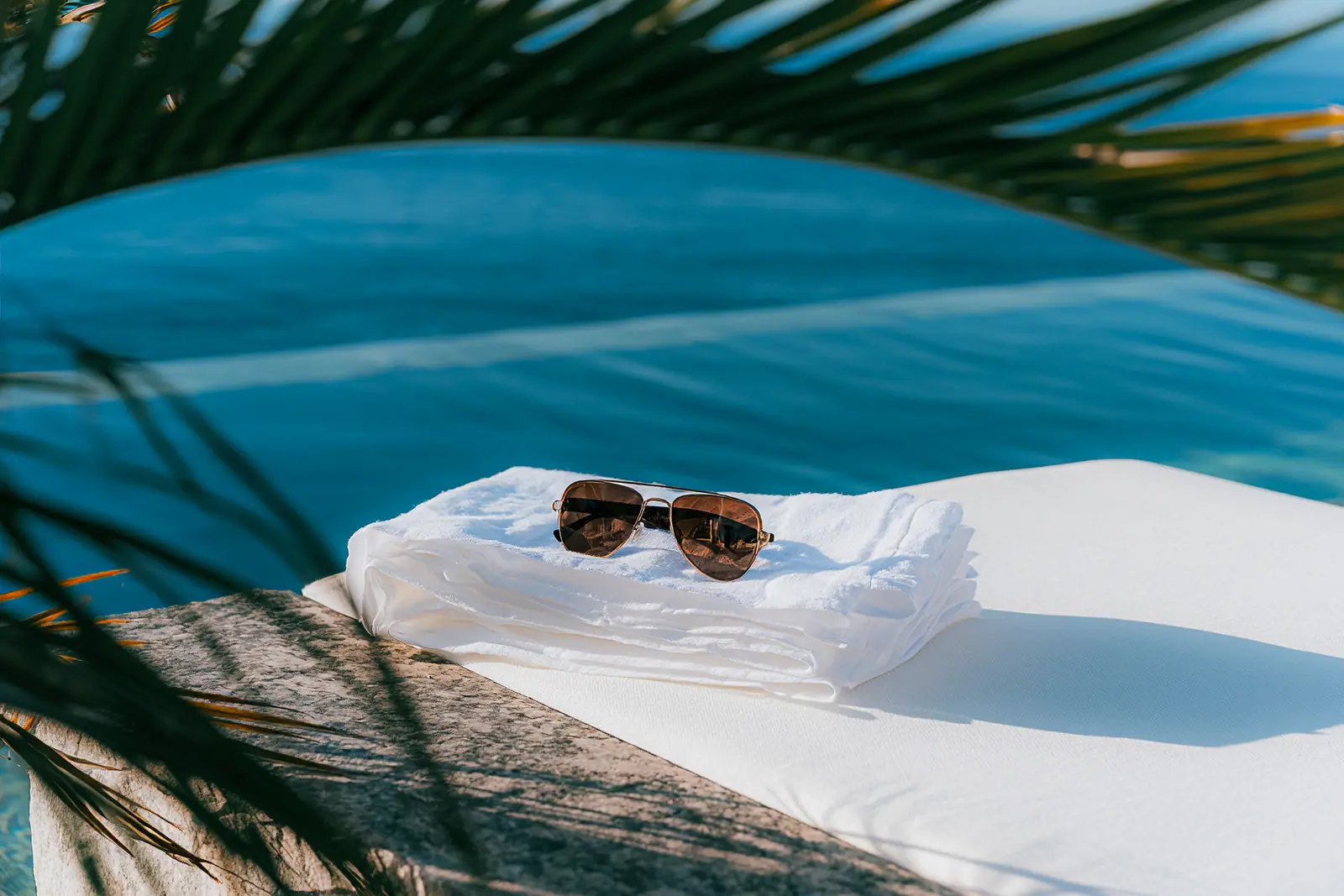 Sunglasses on a folded white towel by a pool