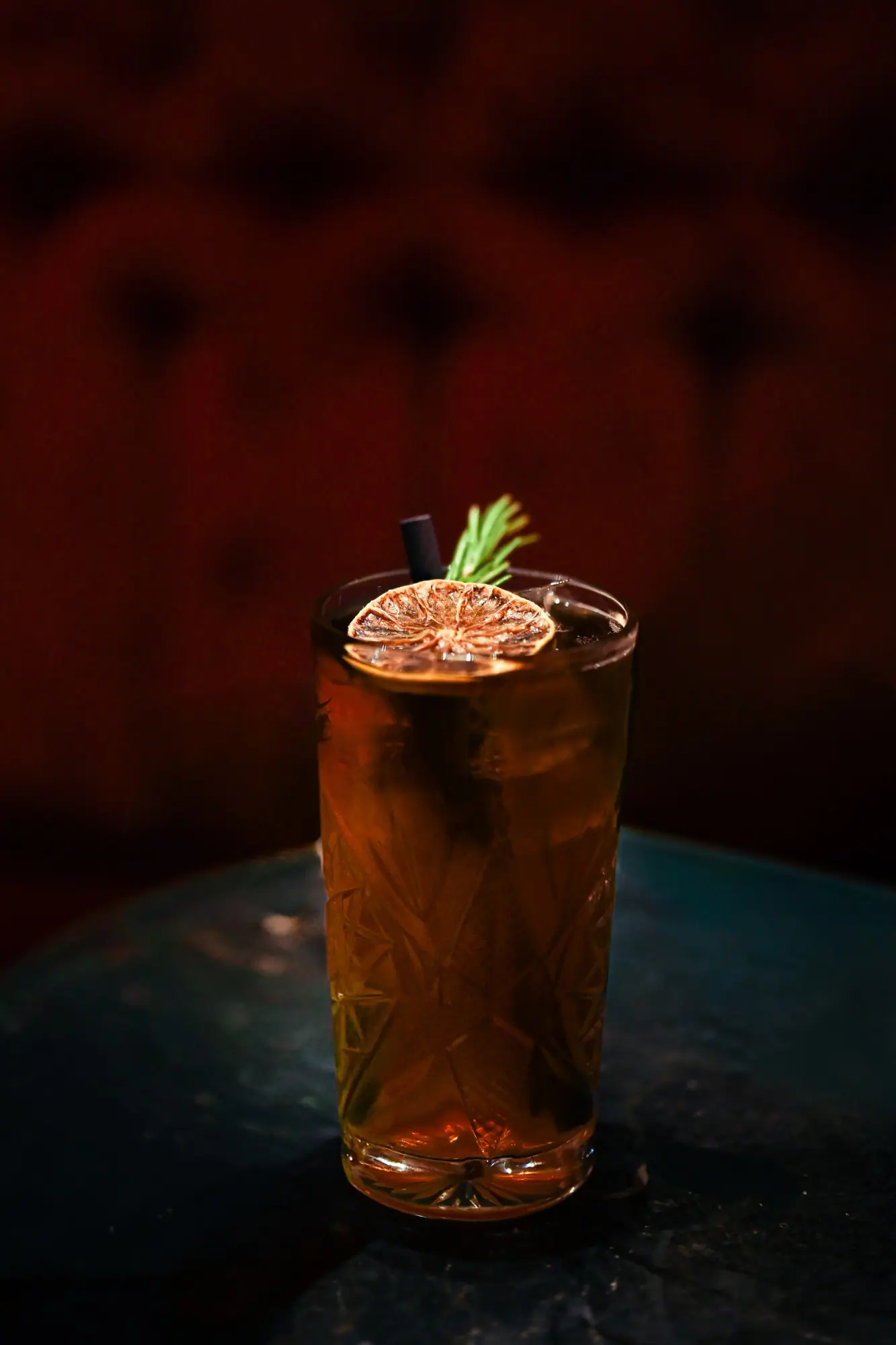 Tall cut glass cocktail with a dried citrus wheel, against deep red velvet