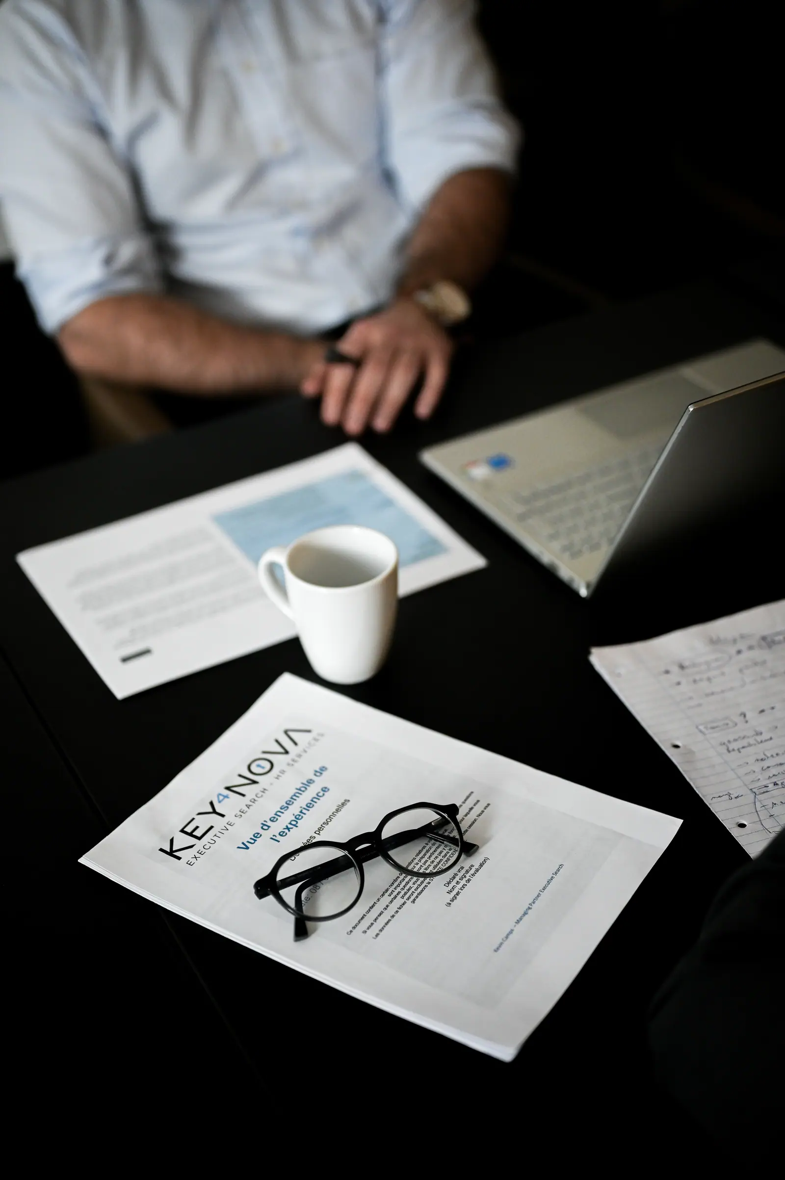 Hands on a desk beside Key4Nova documents, glasses and a coffee cup